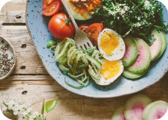 A meal including hard boiled eggs, radishes, tomatoes, and salad, on a plate with a fork.